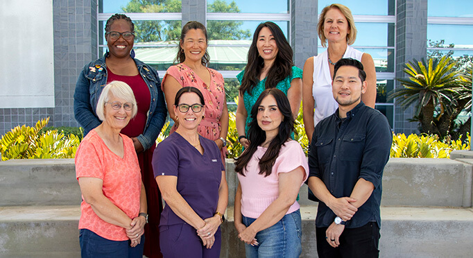 Group of eight diverse team members posing outdoors in two rows, smiling at the camera.