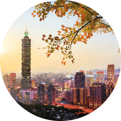 Circular cropped view of the Taipei skyline at sunset with Taipei 101 prominent, framed by orange autumn leaves in the foreground.