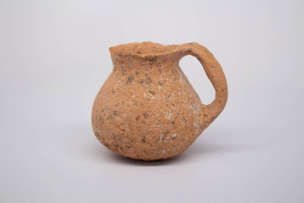 Small ceramic jug with one handle connecting the mouth to the body.
