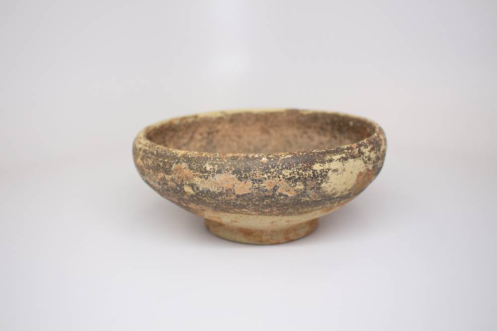 Weathered and encrusted ceramic bowl with a small foot.