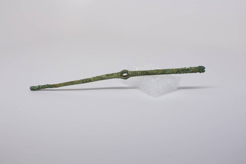Thin brooch with hole in the center that is greened from rust.