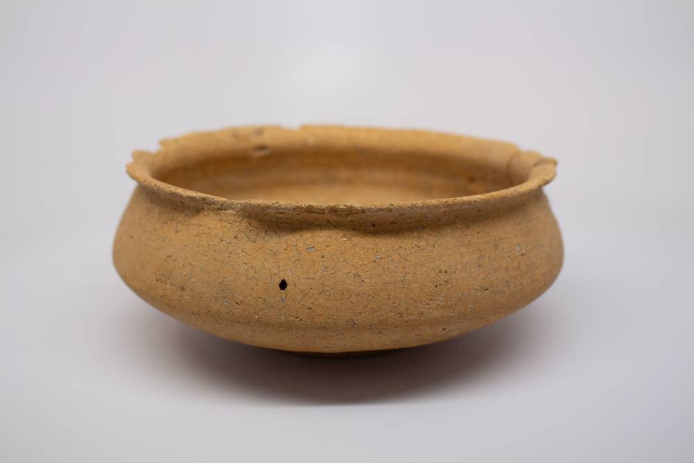Brown ceramic bowl with small foot and chipped curved lip.