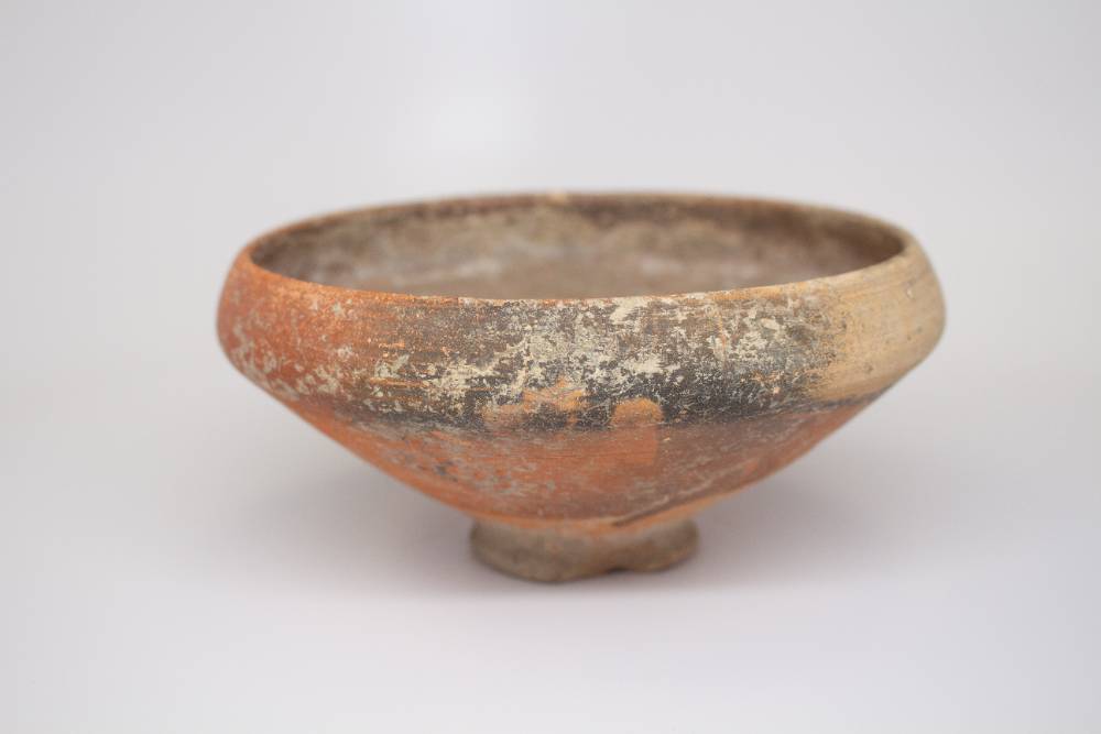 Coroded ceramic bowl with small foot and a beveled lower half.