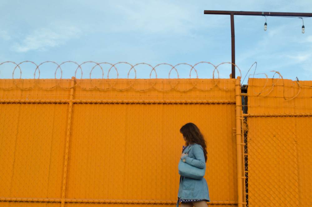 Woman with a purse standing in front of bright yellow gate.