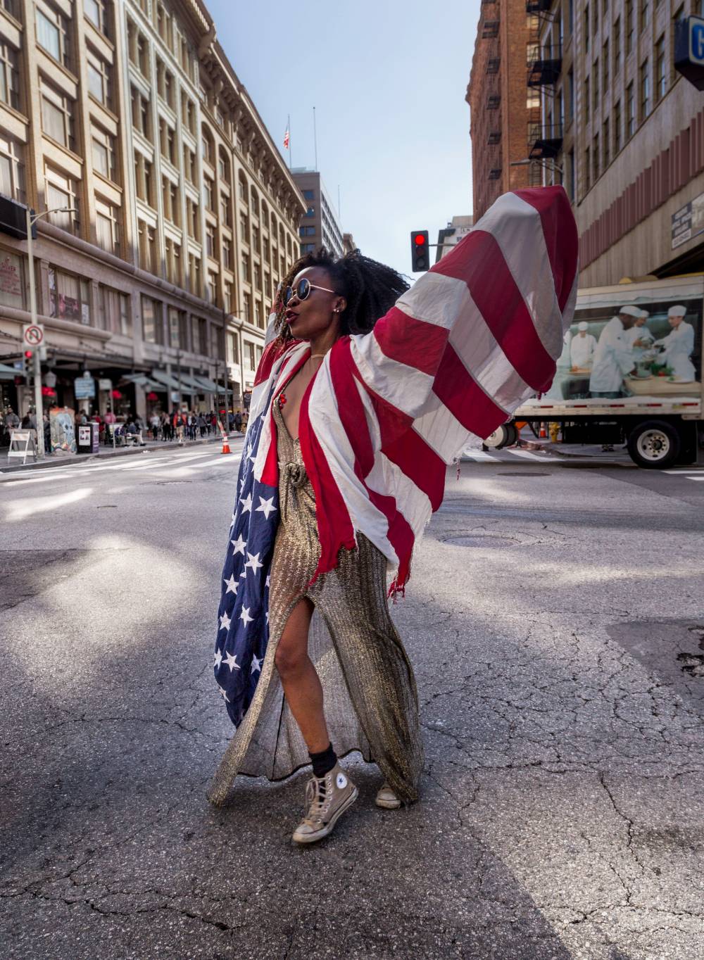 Woman with American flag drapped on her lifted arms in front of cityscape.
