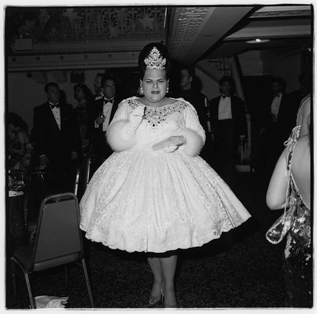 Drag queen in white ball gown and tall tiara.