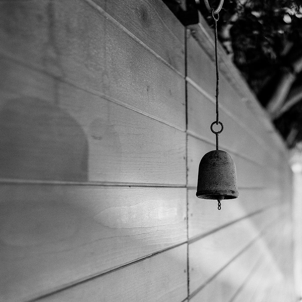 A bell hanging against a wooden fence.