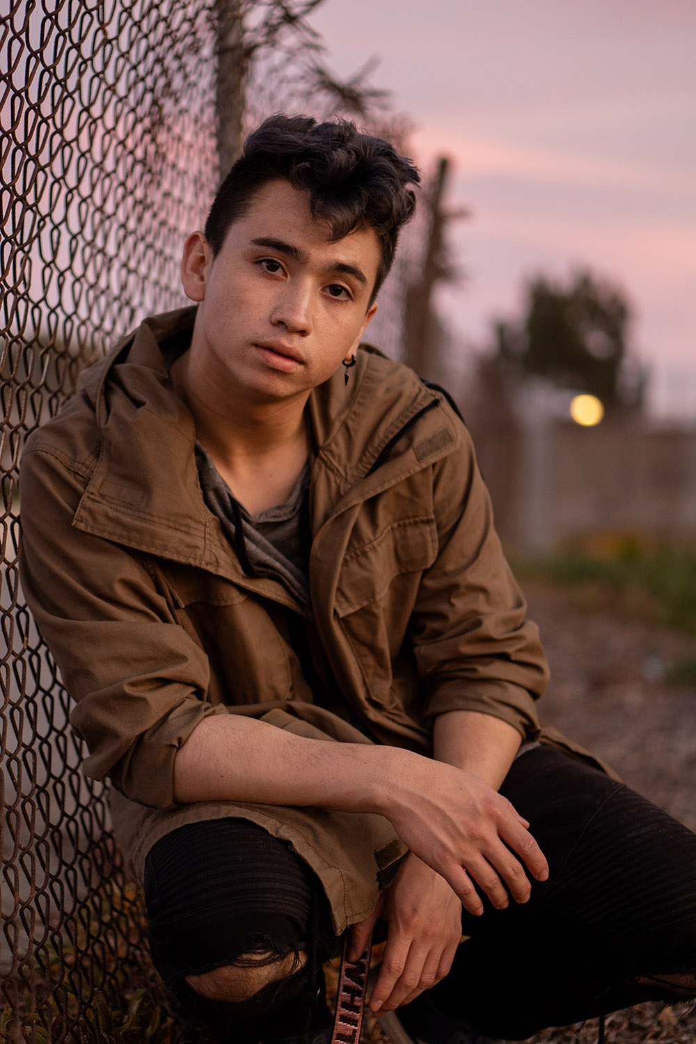 A boy sitting against a chain link fence