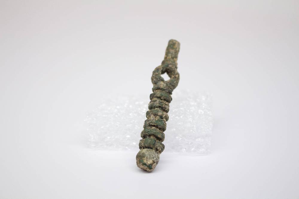Small brooch with hole on top half and layered pattern on bottom half.