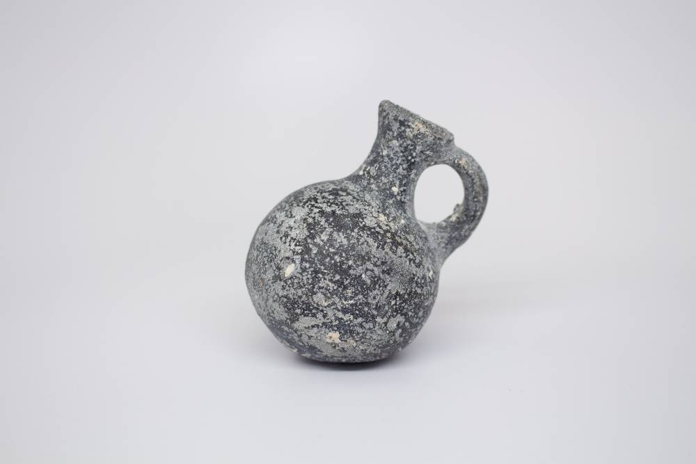 Small gray jug with medium-sized neck and handle connecting neck and body.