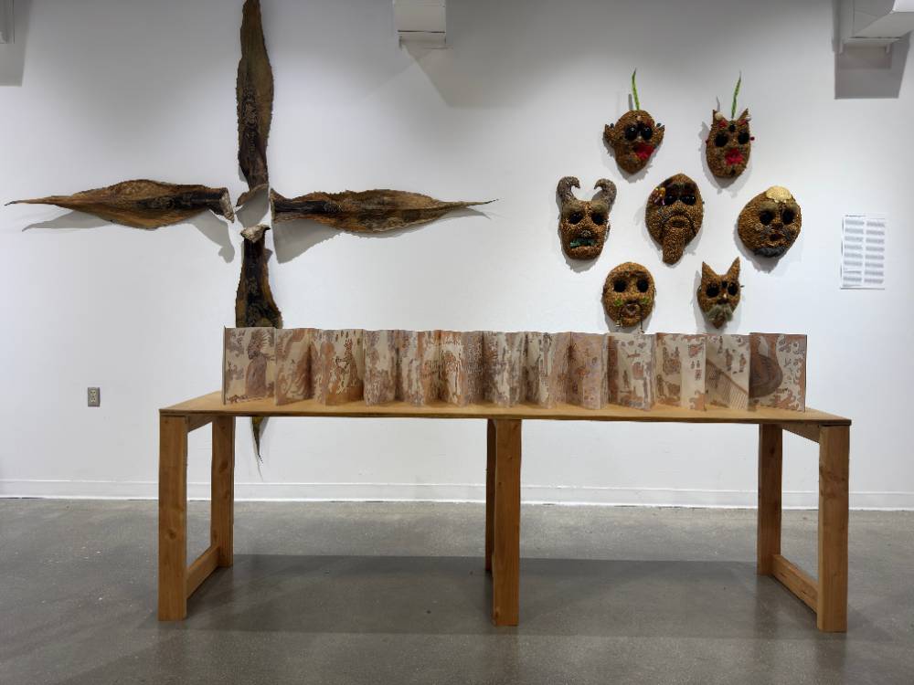 A table with codex, a cross of maguey leaves, and sawdust masks