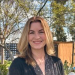 Elisa Coburn smiling and wearing a black cardigan surrounded by trees.