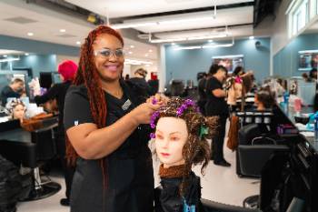 Cosmetology student performing hairstyle on a mannequin head.