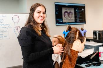 Cosmetology student performing a hairstyle on a mannequin.